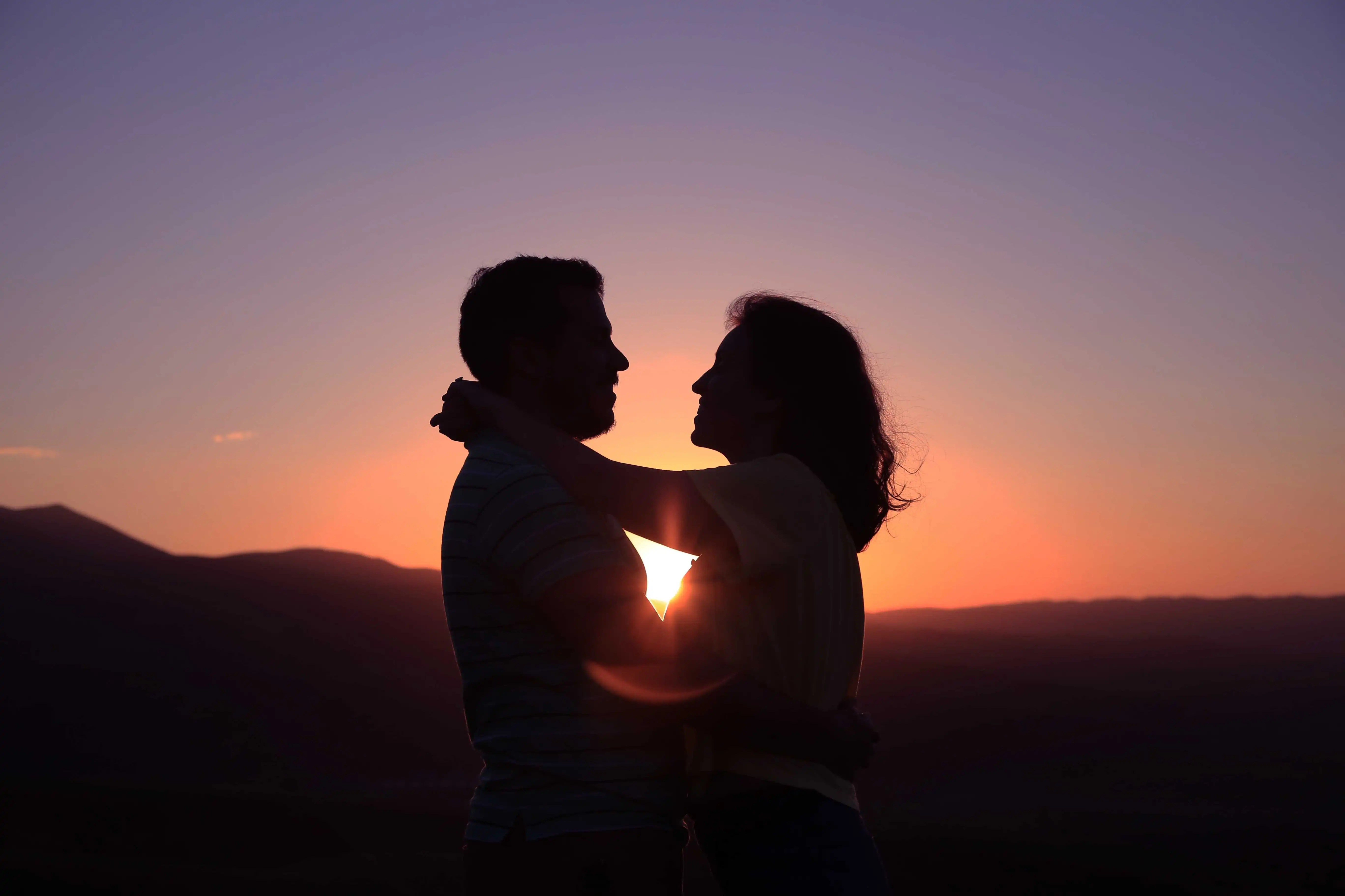 a couple holding hands at the beach as the sun sets
